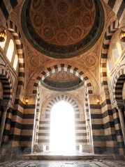 Obraz premium A grand interior view of an ancient mosque or palace with black and white striped walls, ornate domes, and a brightly lit archway.