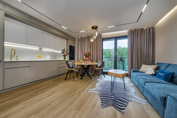 Salon w nowoczesnym apartamencie z beżowym  aneksem kuchennym z drewnianym stołem zastawionym kwiatami i śniadaniem © arteffect.pl