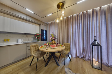 Salon w nowoczesnym apartamencie z beżowym  aneksem kuchennym z drewnianym stołem zastawionym kwiatami i śniadaniem © arteffect.pl