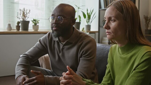 Tilt up medium shot of Black middle aged man and Caucasian middle aged woman arguing during therapy session, man walking away while woman crying. For mental health and relationship counseling ads
