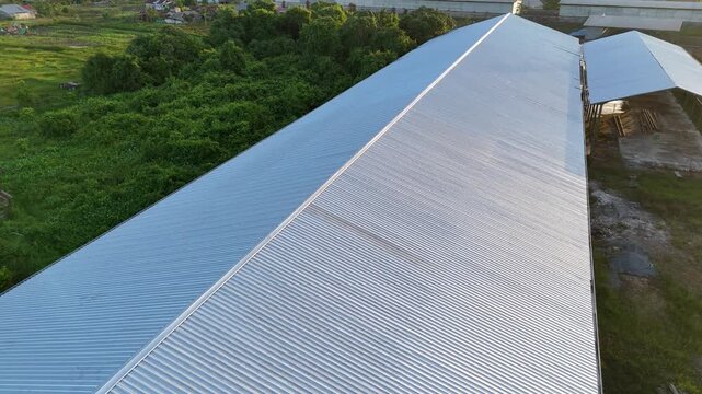 An aerial view from the roof of a metal warehouse with corrugated panels overlooking a green field and an industrial storage area
