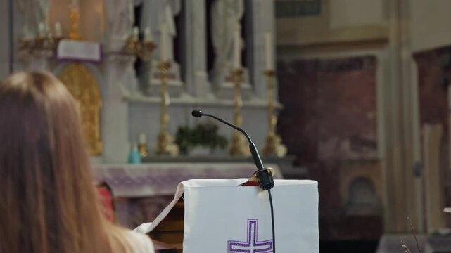 Woman lector in the Catholic Church, standing behind the pulpit and reading Scripture on a microphone, to the congregation at Mass.