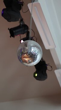 Silver mirror disco ball hanging from a ceiling near stage lighting equipment and modern fixtures, suggesting a party or entertainment venue