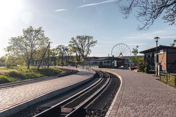 Fototapeta premium View of the narrow-gauge railway station platform and train tracks with a Ferris wheel visible in the background in Sellin, Ruegen island, Germany.