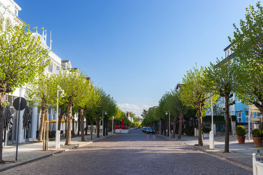 Street view looking down the beautiful tree-lined Wilhelmstrasse avenue, flanked by historic white resort architecture in the seaside town of Sellin, Germany.