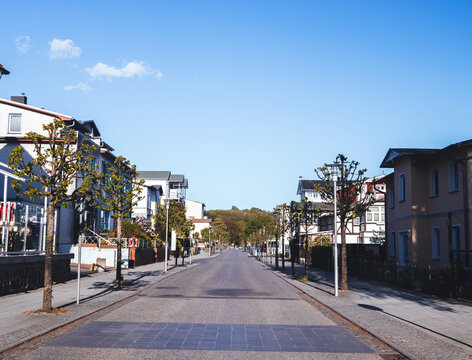 View down a quiet, tree-lined road featuring charming residential houses and traditional resort architecture in Sellin on Ruegen island, Germany.