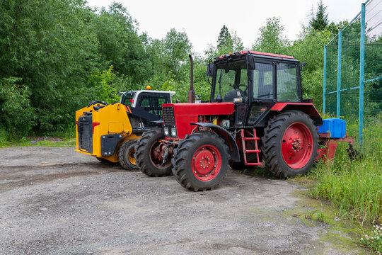 Red tractor and yellow skid steer loader parked outdoors