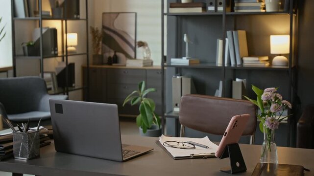Empty therapist office desk featuring laptop, clipboard with glasses, and smartphone on stand. Workspace setup represents professional online counseling and mental health services