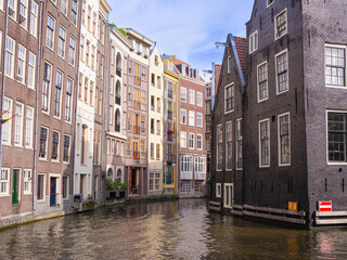 Obraz premium Amsterdam Damrak and Kop Zeedijk narrow canal framed by tall heritage houses, colorful facades and black brick waterfront building, summer travel view of old city architecture