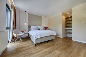 Sypialnia w nowoczesnym apartamencie z dużym  łóżkiem, fotelami, kwiatami i beżową szafą © arteffect.pl