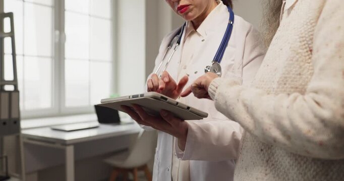 Doctor and senior woman consultation with tablet. At the clinic they review healthcare results, discuss diagnosis and agree on clear treatment choices. Focus on supportive medical advice.
