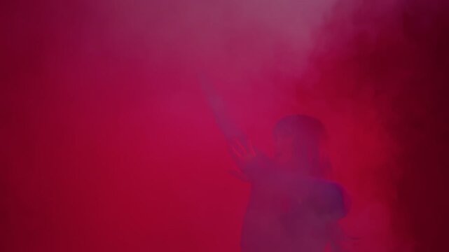 Modern dance performer with raised arms in red smoke