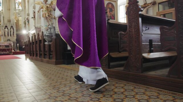Catholic priest carrying and swinging a burning metal thurible on chains while walking through the church aisle, blessing and purification.