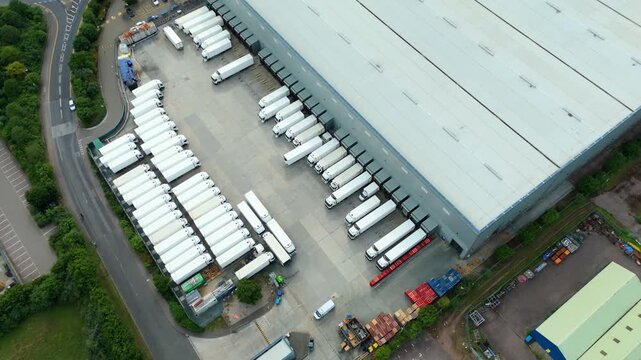 Aerial view of a large logistics warehouse facility with rows of parked semi-trailers and loading bays in Hoddesdon, England, United Kingdom.