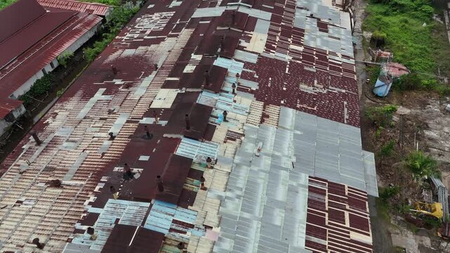 A sweeping aerial view from a drone showing the vast roof of an abandoned factory, covered with rusty metal panels and dotted with numerous smokestacks.