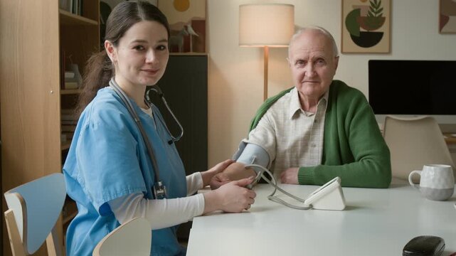 Portrait of young female nurse measuring blood pressure of senior man using digital tonometer and looking at camera. For senior care services