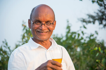 Fototapeta premium Senior cheerful man holding a glass of alcohol in his hand, ready to drink it.