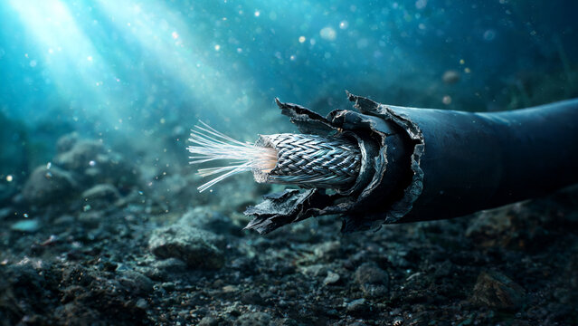 Damaged underwater communication cable with exposed wires and frayed insulation resting on the ocean floor, illuminated by rays of sunlight filtering through the water