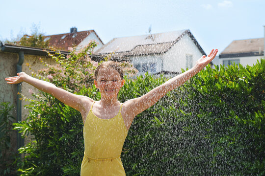 A cheerful child plays with water sprinklers in the garden during the summer. Creatively watering the garden&mdash;with fun and high spirits. An authentic, real little girl.