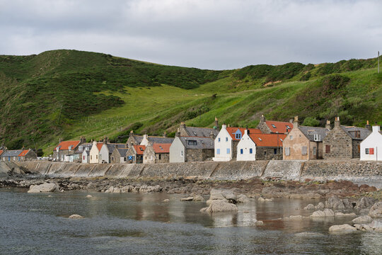 Crovie Fishing Village houses along the rocky shoreline, framed by gentle green hills under a cloudy sky