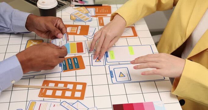 Creative team collaborating on UX and UI design using wireframes, interface components, color palettes, and planning materials to develop digital products through design thinking and teamwork.