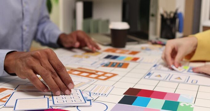 Creative team collaborating on UX and UI design using wireframes, interface components, color palettes, and planning materials to develop digital products through design thinking and teamwork.