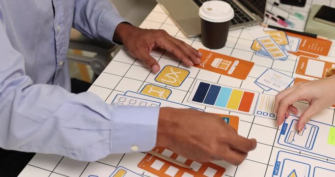Creative team collaborating on UX and UI design using wireframes, interface components, color palettes, and planning materials to develop digital products through design thinking and teamwork.
