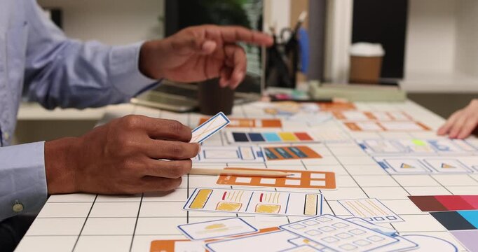 Creative team collaborating on UX and UI design using wireframes, interface components, color palettes, and planning materials to develop digital products through design thinking and teamwork.