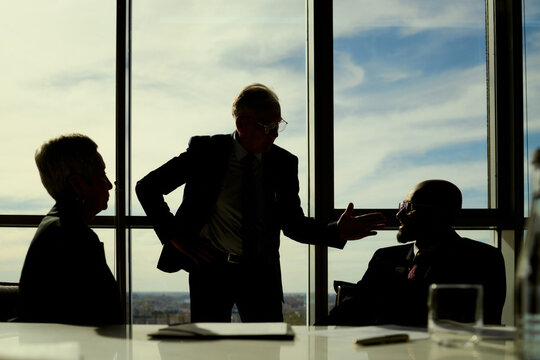 Wide shot of senior businessman leading oil industry meeting with colleagues, discussing strategy and partnership decisions. Useful for energy sector leadership, corporate planning, negotiation