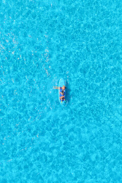 Vertical aerial drone view of friends having summer fun on SUP boards, surfing and jumping into the sea waves. Group of people playing and relaxing together in the turquoise water.