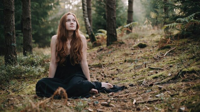 Redheaded woman meditating in forest