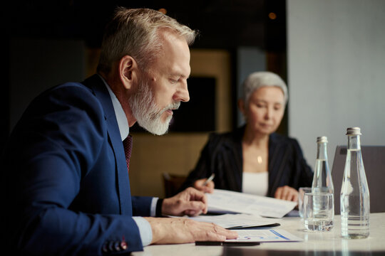 Middle aged business executives reviewing documents during oil industry meeting, discussing strategy and financial planning. Useful for energy sector leadership, corporate planning marketing
