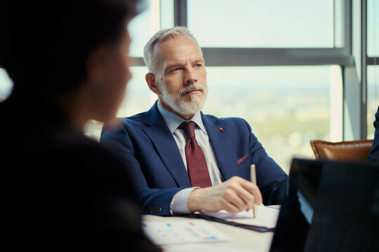 Middle aged Caucasian businessman leading oil industry meeting, reviewing reports and taking notes during strategy discussion. Useful for energy sector leadership, corporate planning, investment