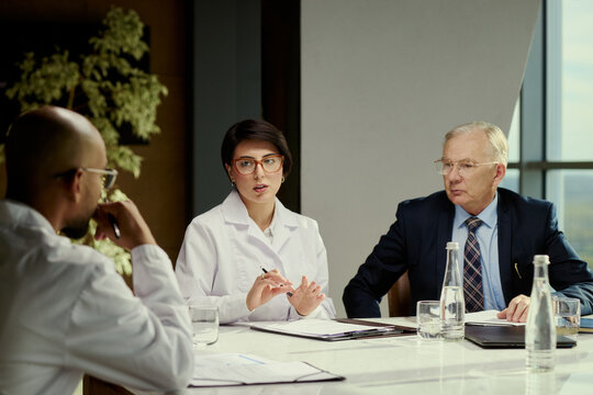 Medium shot of diverse doctors and senior businessman discussing treatment strategy during meeting. Suitable for healthcare management, medical consulting, insurance communication