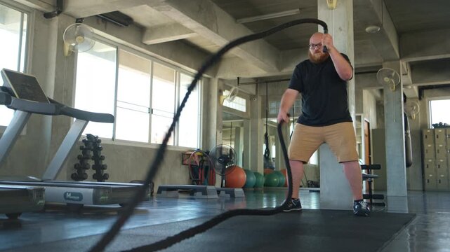 Overweight man performing battle rope training to improve fitness and build strength in a gym
