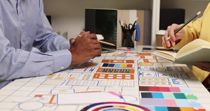 Creative team collaborating on UX and UI design using wireframes, interface components, color palettes, and planning materials to develop digital products through design thinking and teamwork.
