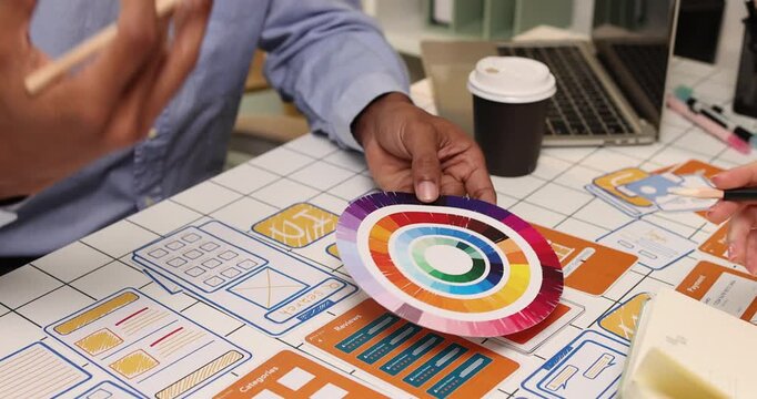 Creative team collaborating on UX and UI design using wireframes, interface components, color palettes, and planning materials to develop digital products through design thinking and teamwork.