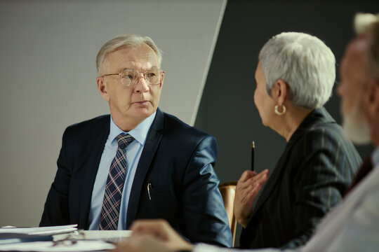 Senior Caucasian businessman listening during boardroom discussion with colleagues, signaling leadership and decision making. Useful for corporate governance, strategy, teamwork marketing