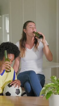 Vertical video: After clinking bottles fan drinking, chatting in kitchen with jersey, ball as fans