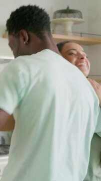 Vertical video: Turning woman reaching partner's hand in kitchen, couple dancing by frying pan