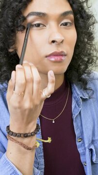 Vertical video: Leaning model using eye brush buffing face at bathroom mirror prepping look maroon