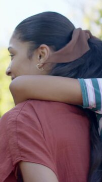 Vertical video: Smiling mom giving piggyback in park as child resting arm for comfort, striped tee