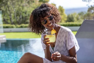 Female sitting poolside wearing shades and white crochet cover-up holding glass with orange slice © wavebreak3