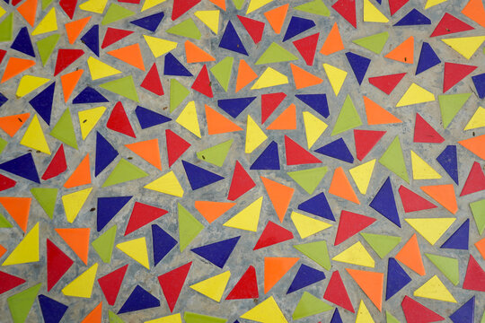 A vibrant geometric mosaic texture showing colorful triangular ceramic tiles set in gray concrete.
