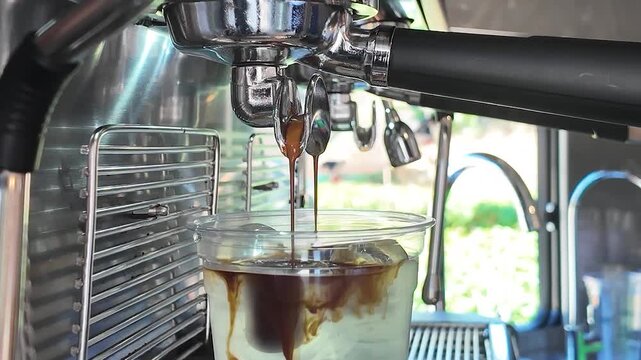 Espresso pouring from a coffee machine into a plastic cup with milk and ice, making iced latte or iced americano in a cafe, close-up of professional brewing process, summer cold beverage.