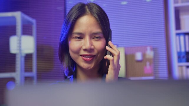 Smiling young Asian businesswoman talking on smartphone in office.