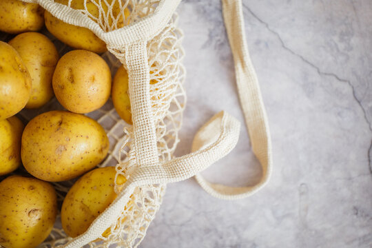 Freshly harvested potatoes in a woven bag resting on a rustic kitchen countertop