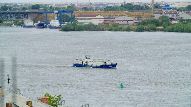 Workboat sailing across wide river near industrial shoreline