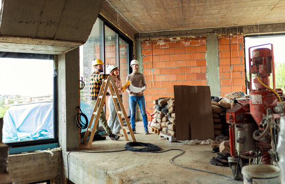 Adult couple discussing building plans with a contractor at a house construction site.