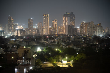 Fototapeta premium Aerial drone wide shot showing cityscape skyscrapers at night in mumbai hyderabad bangalore with smaller houses in foreground